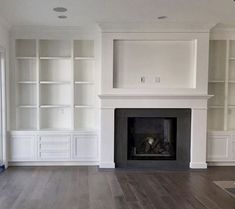 an empty living room with white bookcases and a fireplace