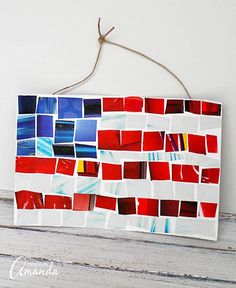 a red, white and blue mosaic tile wall hanging on a wooden board with twine