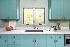 a kitchen with blue cabinets and white counter tops is pictured in this image, there are two windows above the sink