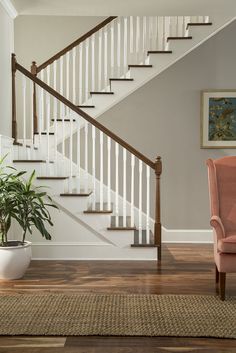 a pink chair sitting in front of a stair case next to a potted plant