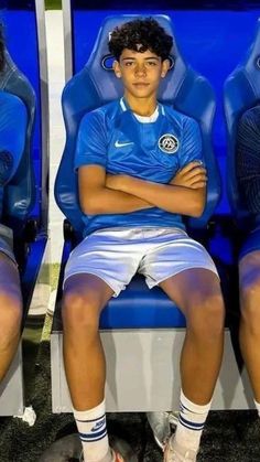 two young men sitting on blue seats with their arms crossed and one man in white shorts