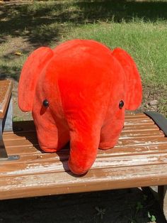 an orange stuffed elephant sitting on top of a wooden bench