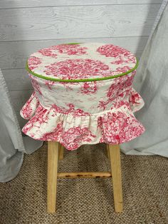 a pink and white flowered chair with ruffled seat cover on the top, sitting in front of a curtain