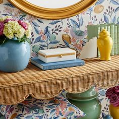 a wicker shelf topped with books and vases next to a wallpapered wall