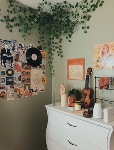 a white dresser sitting next to a wall covered in pictures and plants on top of it