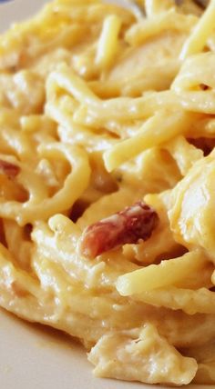 a white plate topped with macaroni and cheese covered in bacon next to a fork