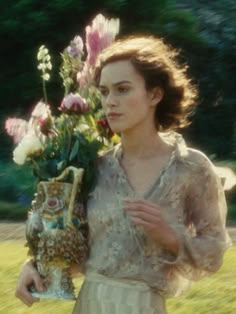 a woman is holding a vase with flowers in it and looking at the camera while standing outside