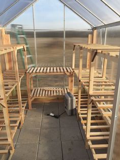 the inside of a greenhouse with several wooden shelves and benches in front of glass walls