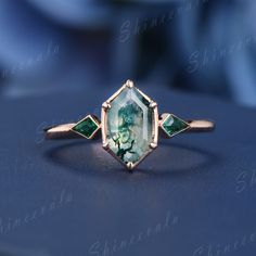 an image of a ring with green stones on it's sides and two diamonds in the middle