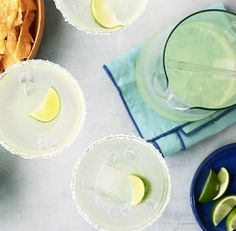 three margaritas with lime slices on the rim next to a bowl of tortilla chips