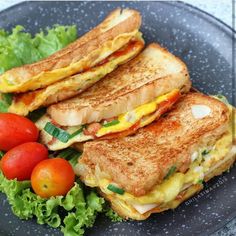 two grilled sandwiches on a plate with tomatoes and lettuce next to them