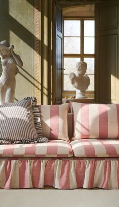 a pink and white striped couch sitting in front of a window next to a statue