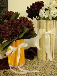 two vases with flowers in them sitting on a counter next to a pair of pencils