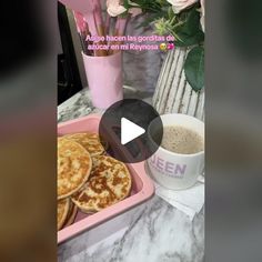 a pink tray filled with pancakes next to a cup of coffee and vase of flowers