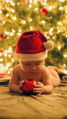 a baby wearing a santa hat on top of a bed next to a christmas tree