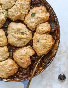 a skillet filled with biscuits and sauce on top of a white countertop next to a spoon