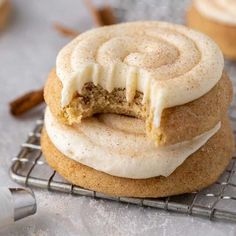 two cookies with frosting and cinnamon on top sitting on a cooling rack next to some cinnamon sticks