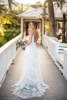 a woman in a wedding dress standing on a bridge holding a bouquet and looking at the camera