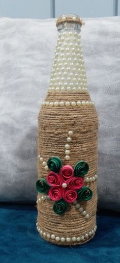 a bottle decorated with flowers and pearls sitting on a blue surface next to a pillow