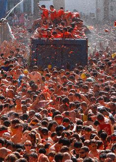 a large group of people standing in front of a truck covered in orange colored water