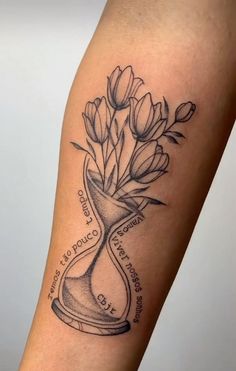 a black and white photo of a tattoo with flowers in a hourglass on the arm