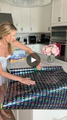 a woman standing in front of a kitchen counter holding up a large sheet of wrapping paper