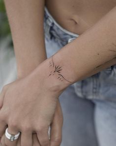 a woman's arm with a small tattoo on her left wrist and a dandelion in the middle