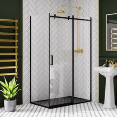 a bathroom with green walls and white tile flooring has a black shower enclosure, gold fixtures, and a pedestal sink