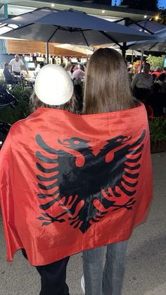 two people are walking down the street with a red and black flag on their back