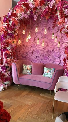 a pink couch sitting in front of a purple wall with flowers on it and lights hanging from the ceiling