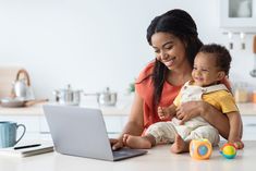 a woman holding a baby while using a laptop computer