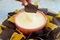 a person dipping tortilla chips into a bowl filled with white sauce and cheese