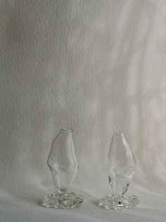 two clear glass vases sitting next to each other on a white cloth covered surface