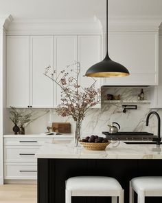 a kitchen with white cabinets and marble counter tops, two stools in front of the island