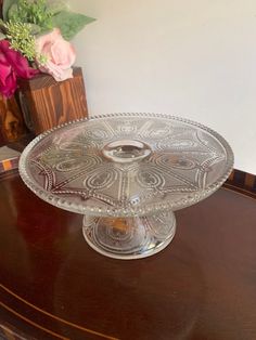 a glass cake plate sitting on top of a wooden table next to a vase with flowers