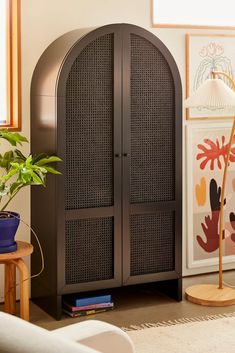 a black cabinet sitting in the corner of a living room next to a potted plant