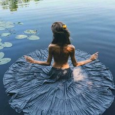 a woman is sitting in the water with her arms spread out and looking at lily pads