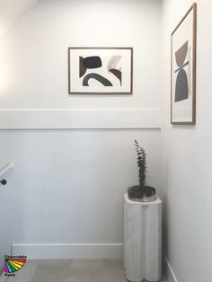 a white wall with two pictures on it and a plant in a vase next to it