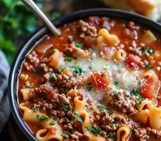 a black bowl filled with pasta and meat soup next to bread on a wooden table