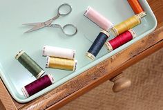 several spools of thread and scissors on a tray with needle tips in them