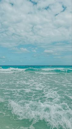 an ocean with waves coming in to shore and blue sky filled with white clouds above