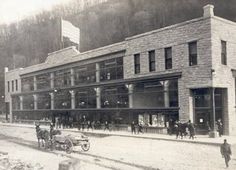 an old black and white photo of people walking in front of a building with horse drawn carriages