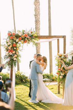 a bride and groom kiss under an arch decorated with flowers at the end of their wedding ceremony