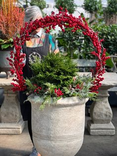 a woman walking past a potted plant with red berries and greenery in it