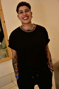 a young man with tattoos and piercings standing in front of a mirror smiling at the camera