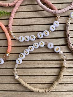 three different necklaces with letters on them sitting on top of a wooden table next to plants