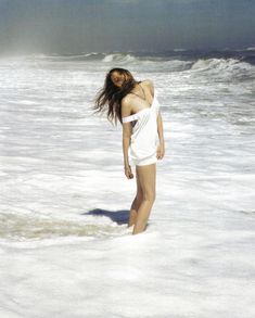 a woman standing in the ocean with her hair blowing in the wind and wearing a white dress