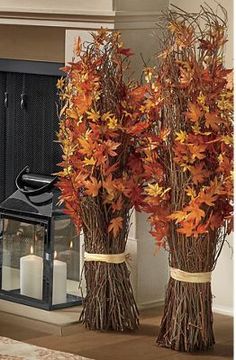 two tall vases filled with leaves next to a candle on the floor in front of a fireplace