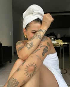 a woman with tattoos on her body sitting in a bathrobe and towel over her head