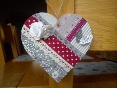 a heart shaped decoration hanging from a wooden post with white flowers and ribbons on it